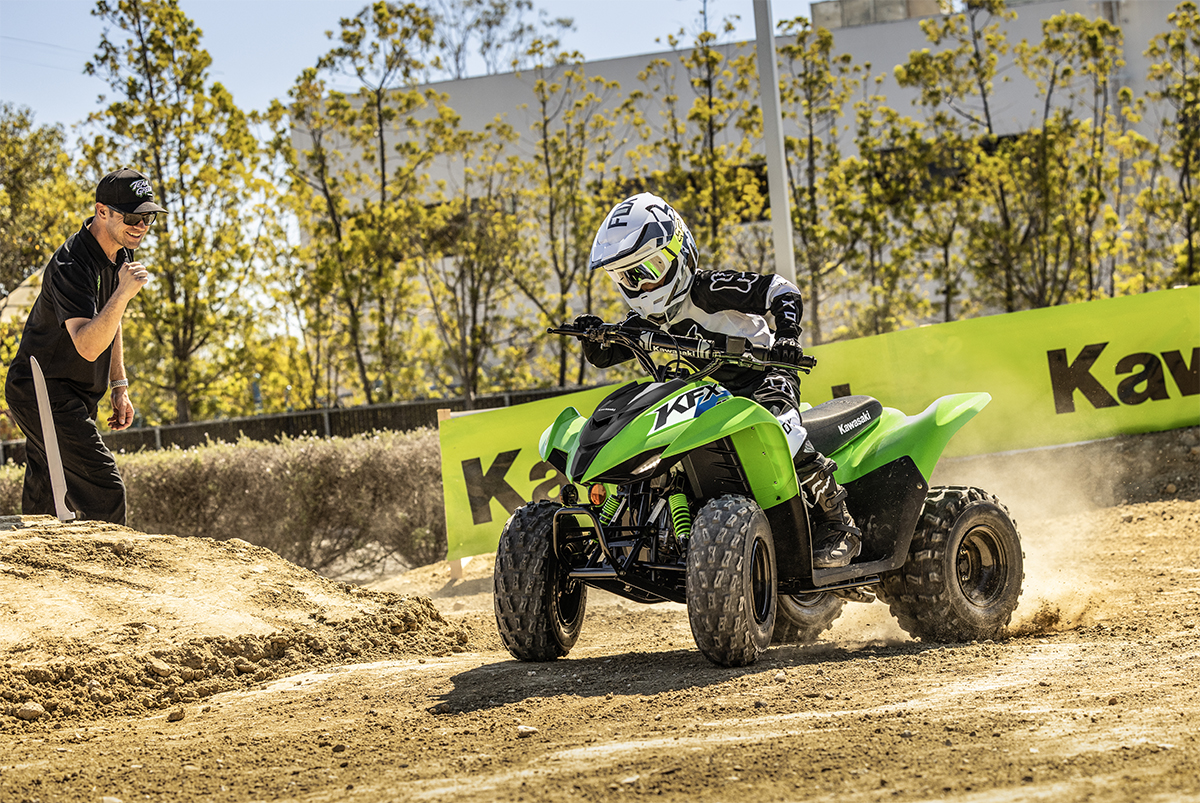 Three-quarter front angle of a person riding a green ATV on a closed course under adult supervision.