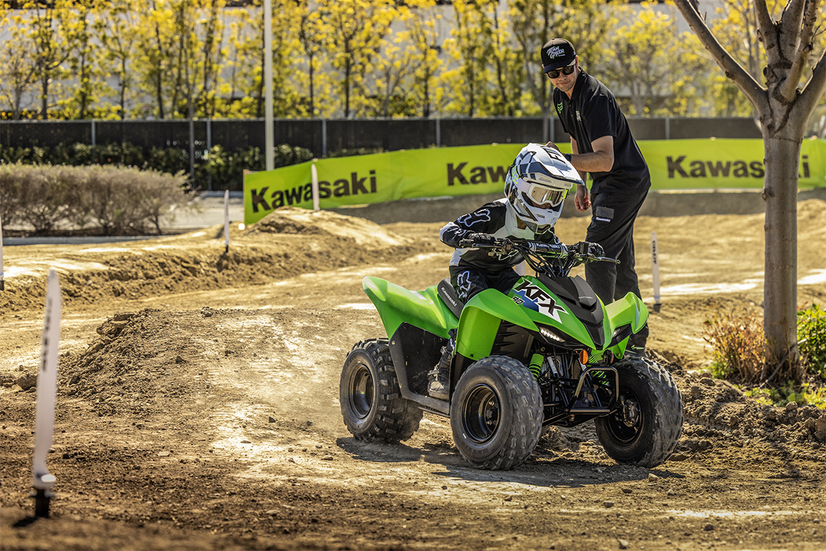 Three-quarter front angle of a person riding an ATV around a bend on a closed course under adult supervision.