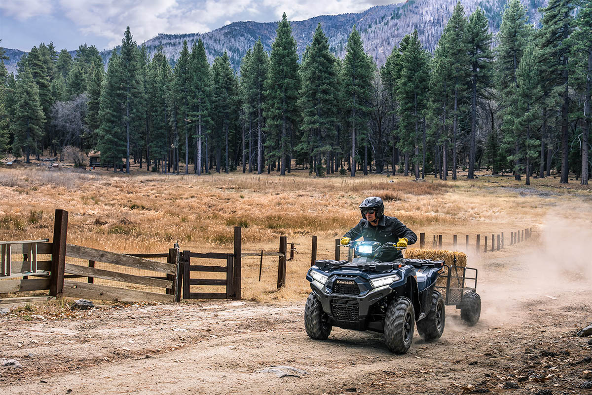 Three-quarter front angle of a person riding an ATV off-road on a large property with a trailer in tow.