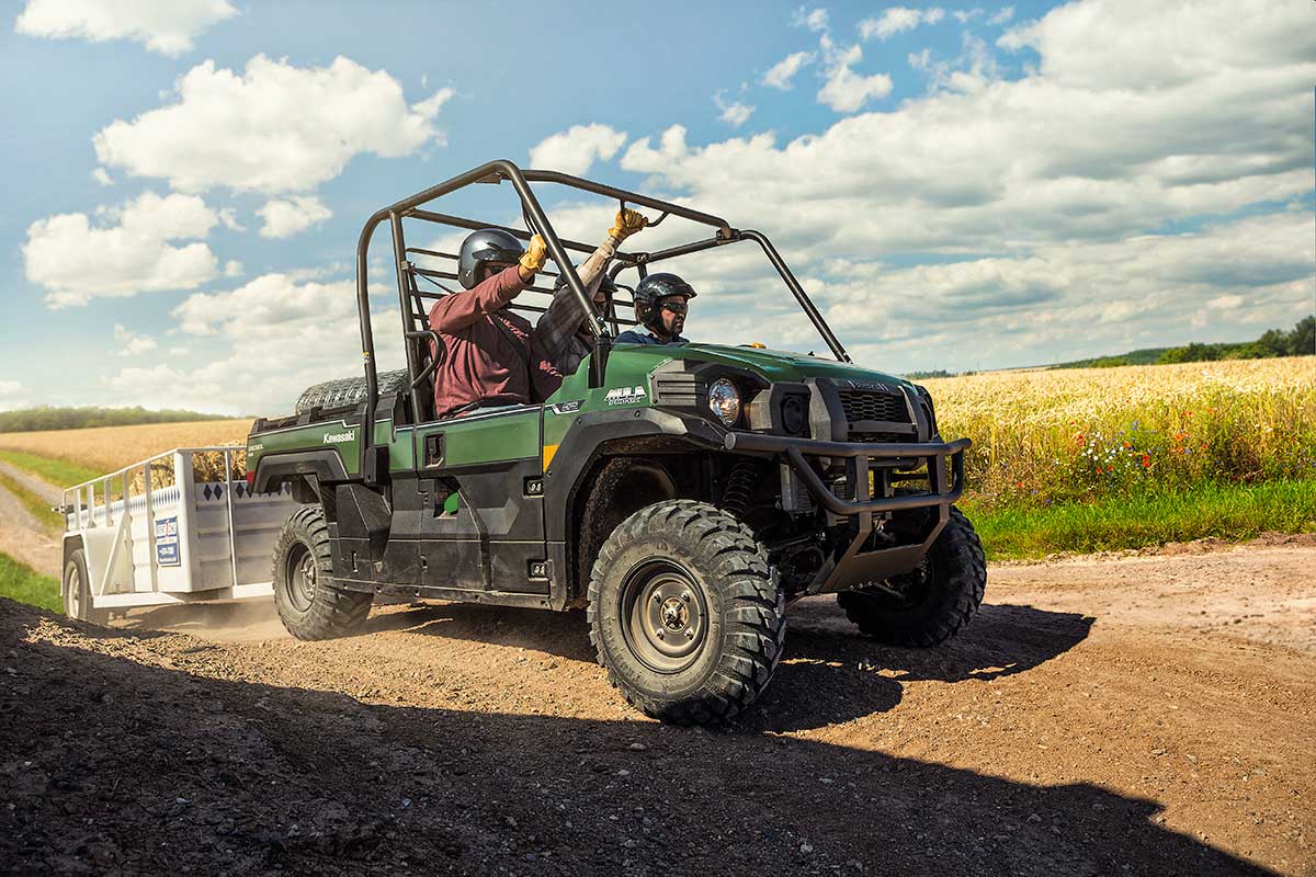 Three-quarter front angle of three people riding in a side x side on a ranch with a trailer in tow.