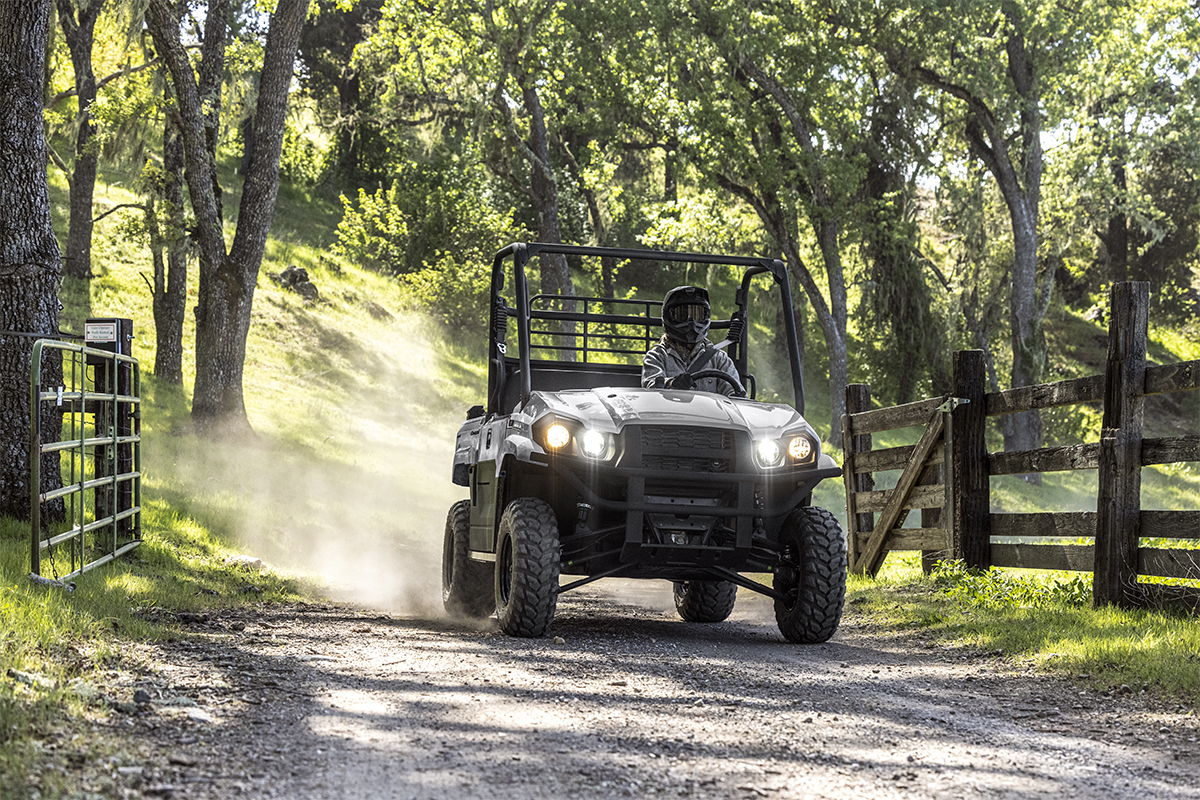 Front angle of a person driving a side x side through a gate on a ranch.