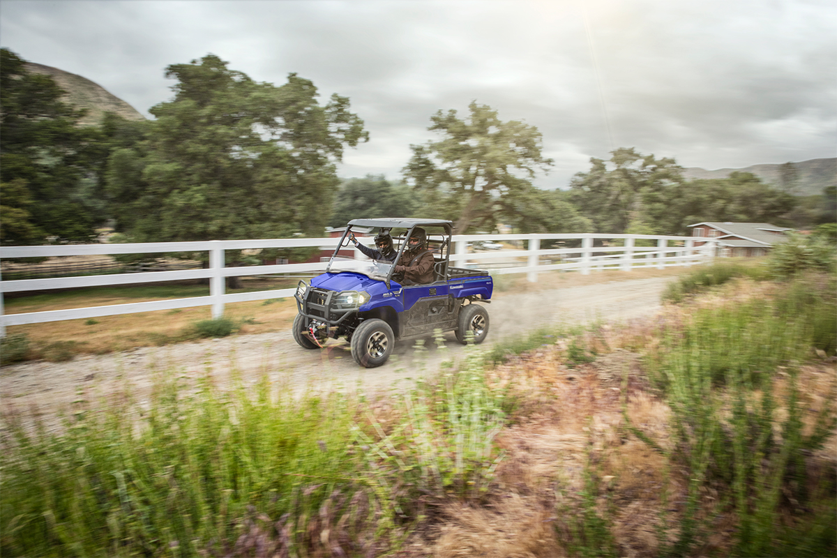 Three-quarter front angle of a person and passenger driving a side x side on a dirt trail.