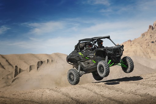 Three-quarter front angle of two people driving a side x side off-road. opens in a new window