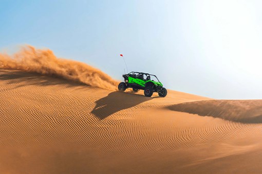 Side angle of a person driving a side x side off-road on top of a dune. opens in a new window
