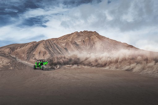 Side angle of a person driving a side x side off-road at the bottom of a large dune. opens in a new window