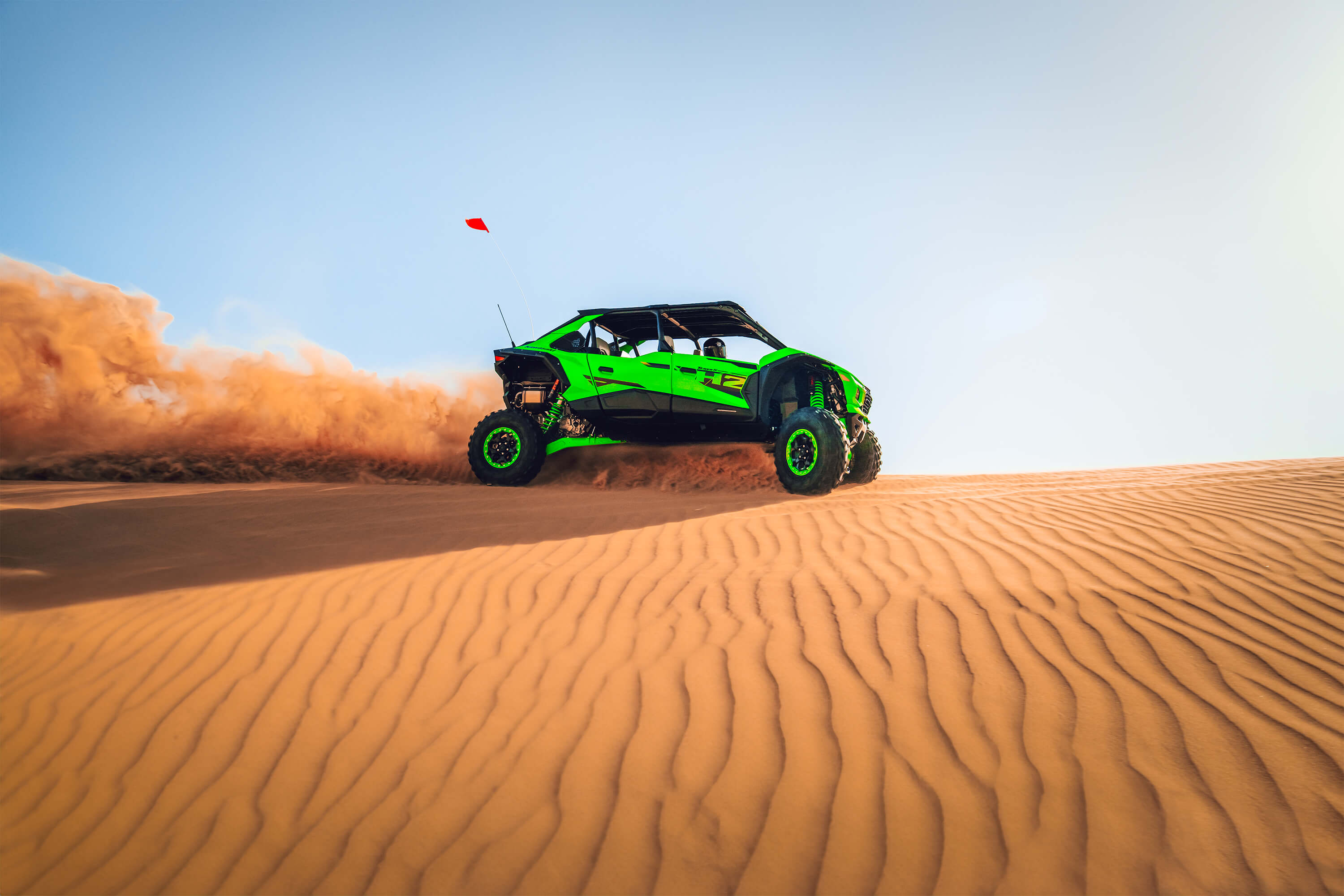 Side angle of a person driving a side x side off-road along the top of a sand dune.