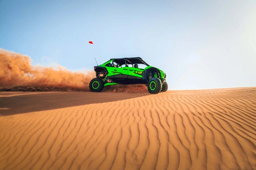 Side angle of a person driving a side x side off-road along the top of a sand dune. opens in a new window