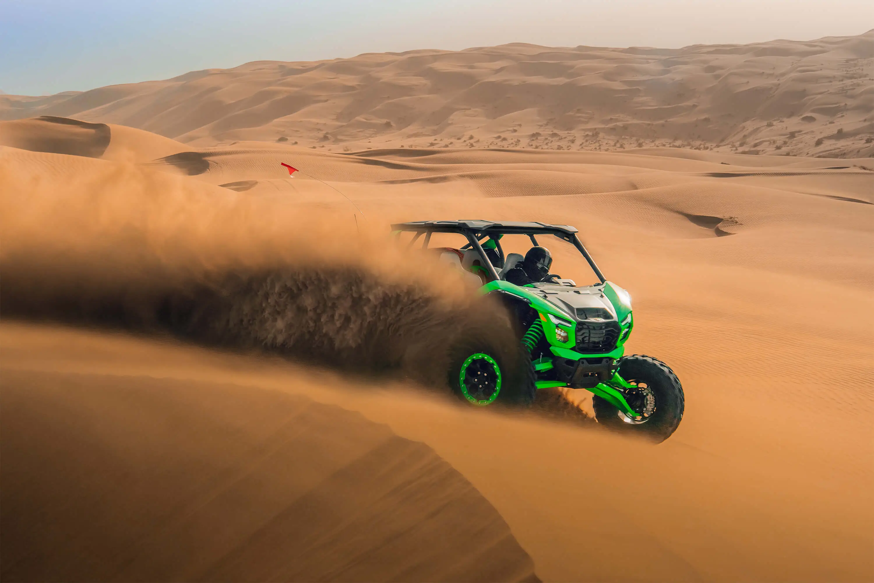 Profile angle of a person driving a side x side off-road kicking up sand.