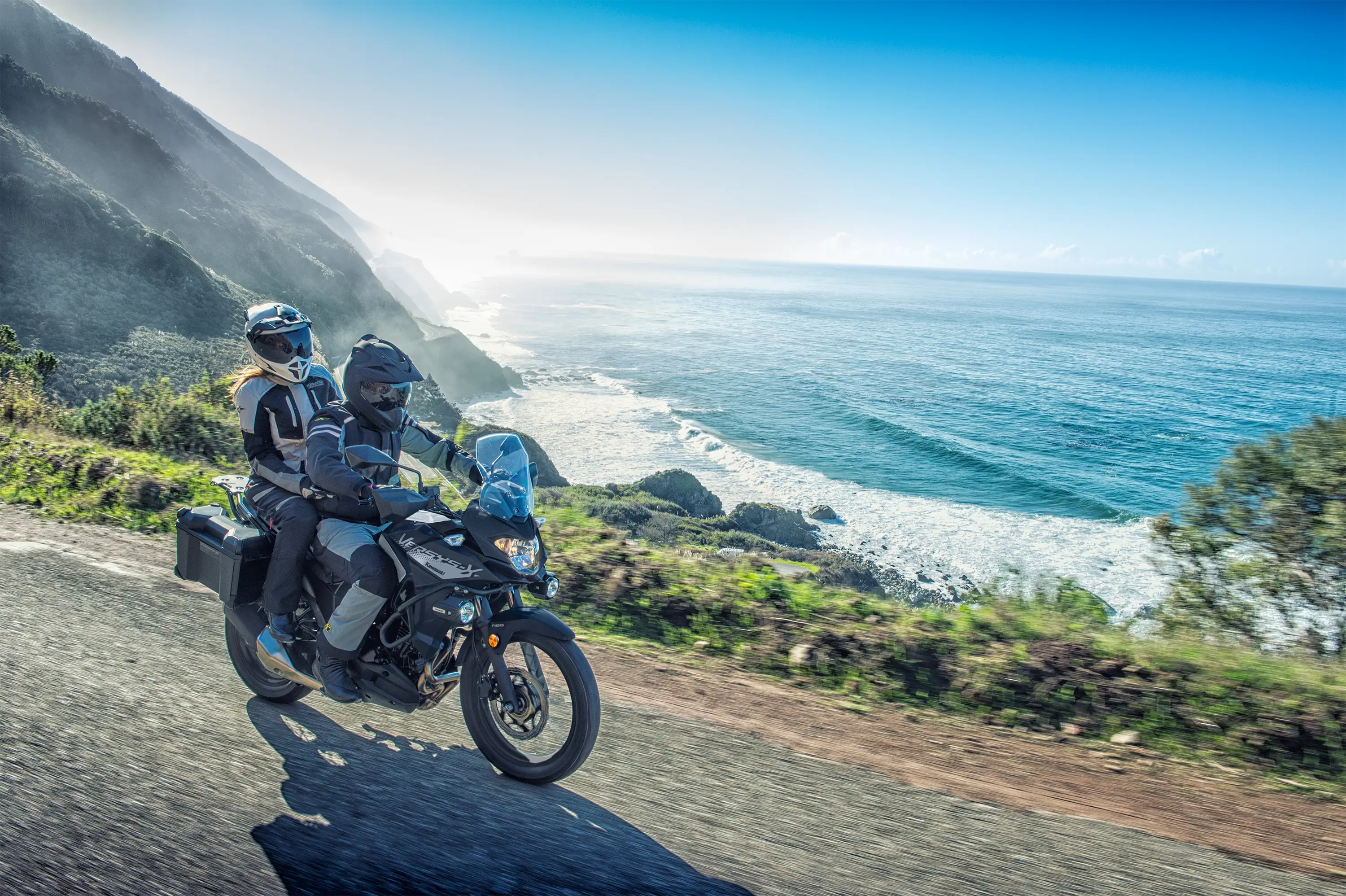 Side angle of a person riding a motorcycle next to an ocean view.