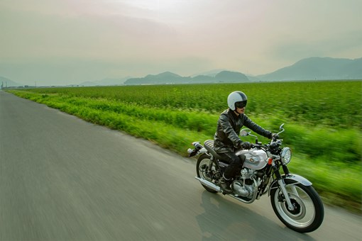 Three-quarter front angle of a person riding a motorcycle next to a field. opens in a new window