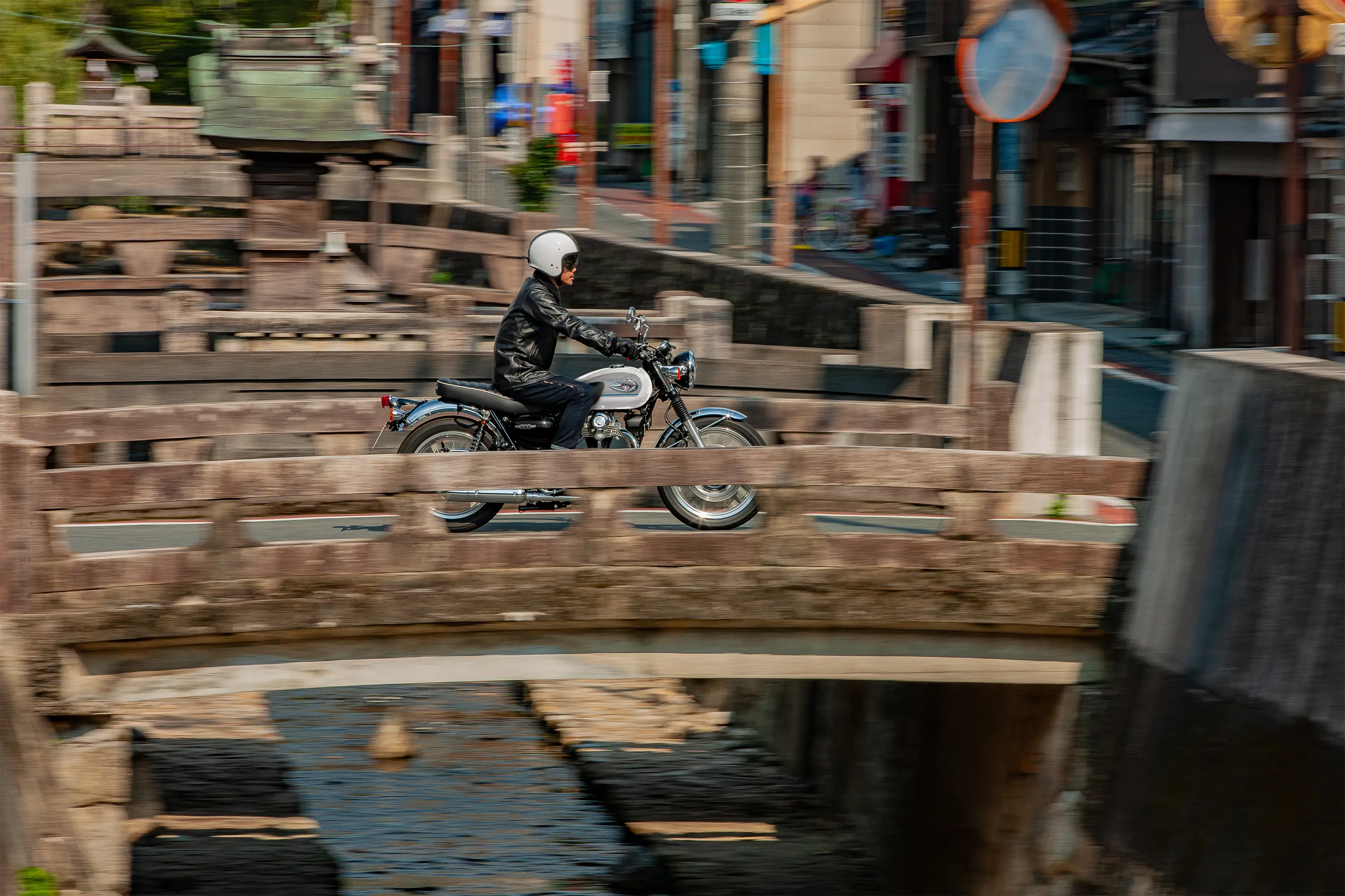 Side angle of a person riding a motorcycle over a bridge.