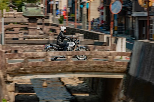 Side angle of a person riding a motorcycle over a bridge. opens in a new window