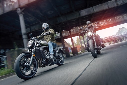 Three-quarter front angle of two people riding motorcycles on the street. opens in a new window