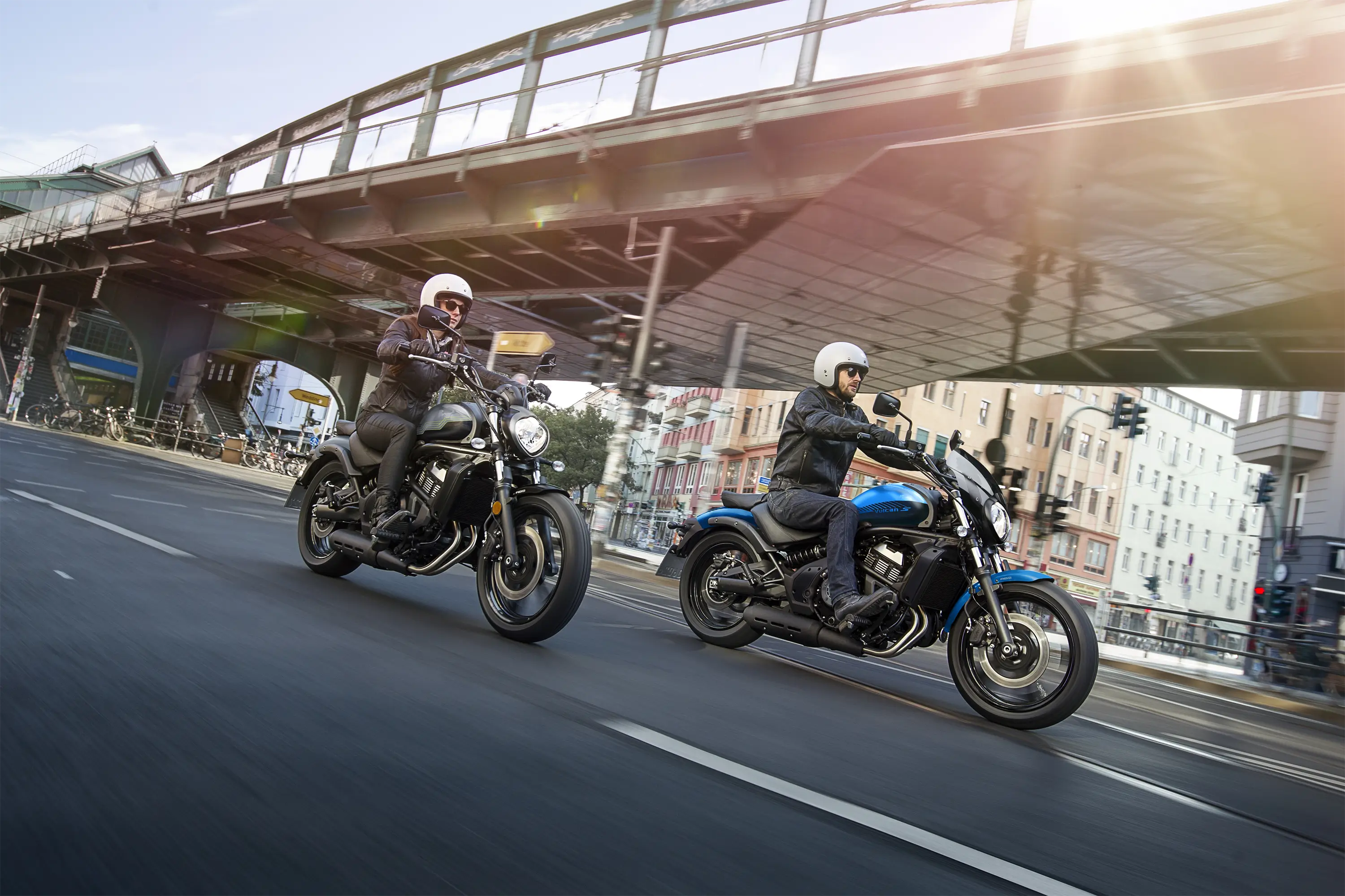 Three-quarter front angle of two people riding motorcycles on the street.