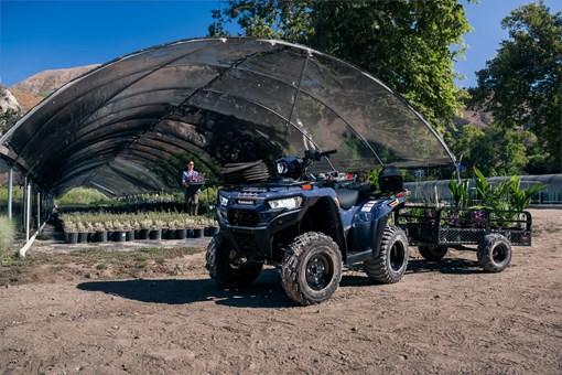 Three-quarter front angle of an ATV parked off-road with a trailer. opens in a new window