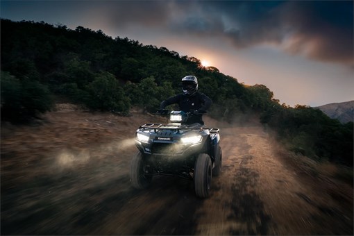 Front three-quarter angle of a person riding an ATV on a trail at sunset. opens in a new window
