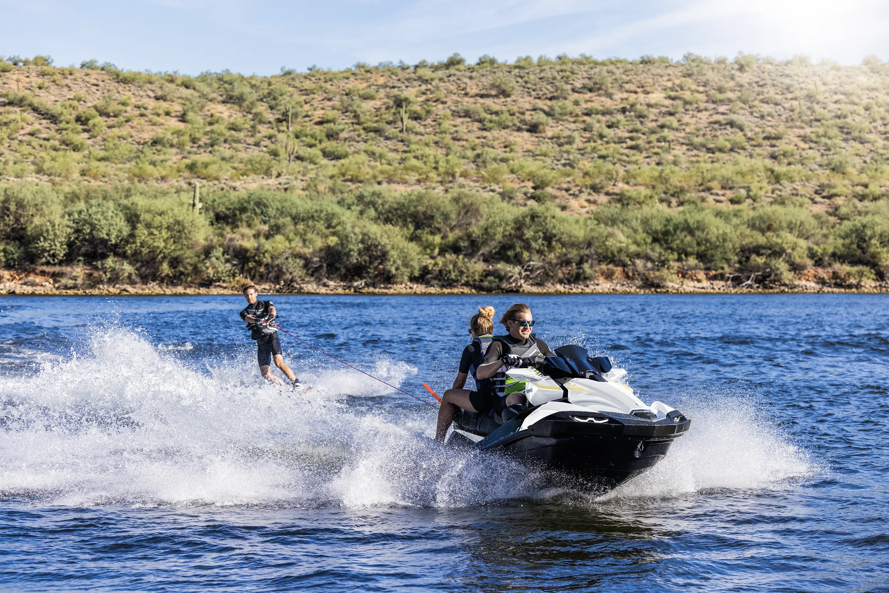 Front angle of a person wake boarding behind a personal watercraft on the water.