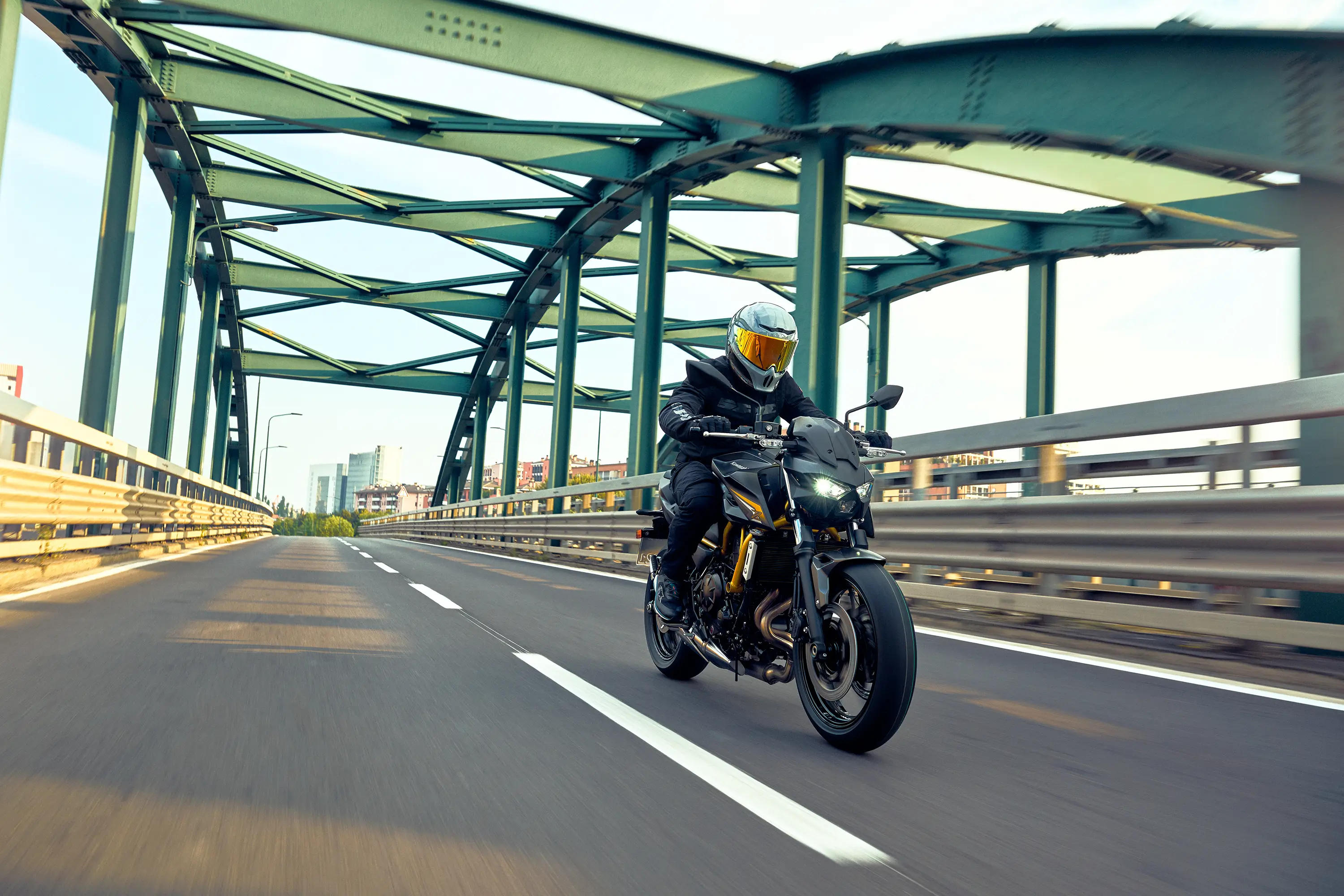 Three-quarter front angle of a person riding a motorcycle on a bridge.