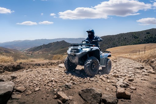 Three-quarter front angle of a person driving an ATV up a ridge. opens in a new window