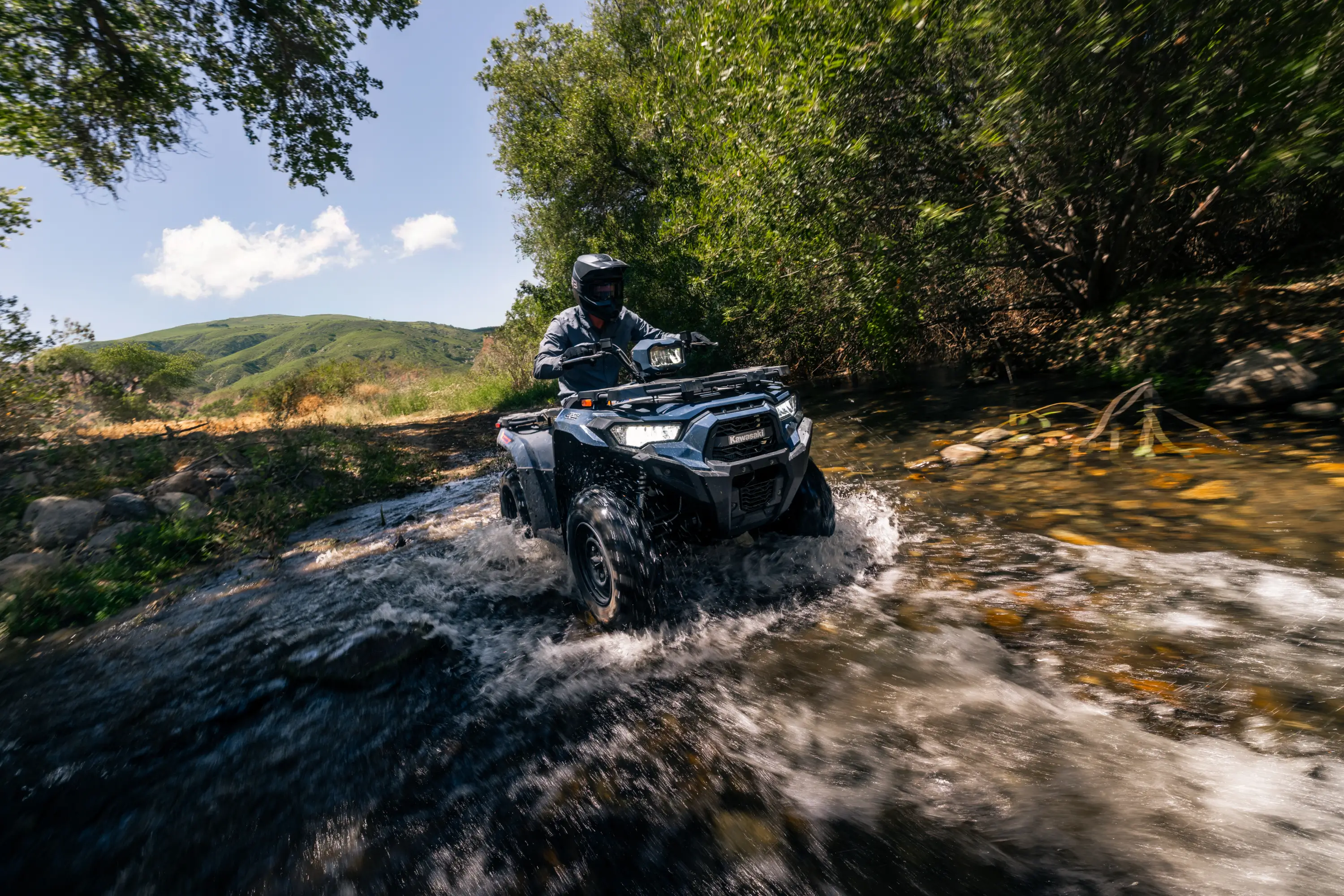 Front angle of a person driving an ATV in a shallow creek.