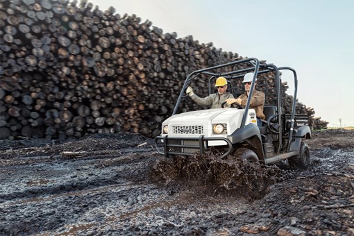 Three-quarter front angle of two people riding a side x side on a jobsite. opens in a new window
