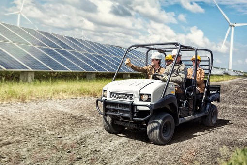 Three-quarter front angle of four people riding a side x side on a jobsite. opens in a new window