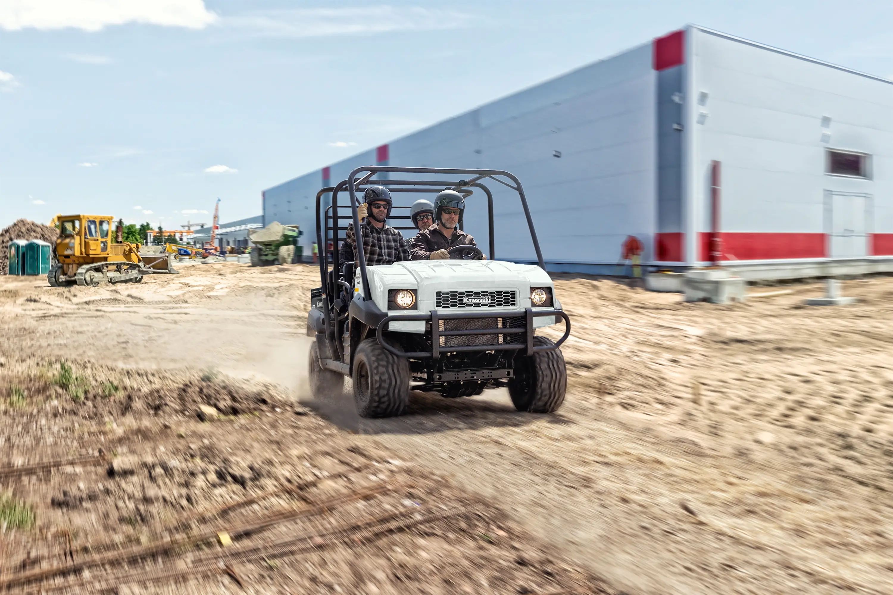 Front angle of three people riding a side x side on a jobsite.