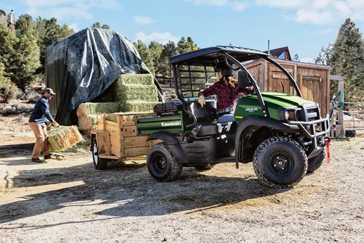 Side view of a person backing up a side x side with a trailer to a stack of hay bales. opens in a new window