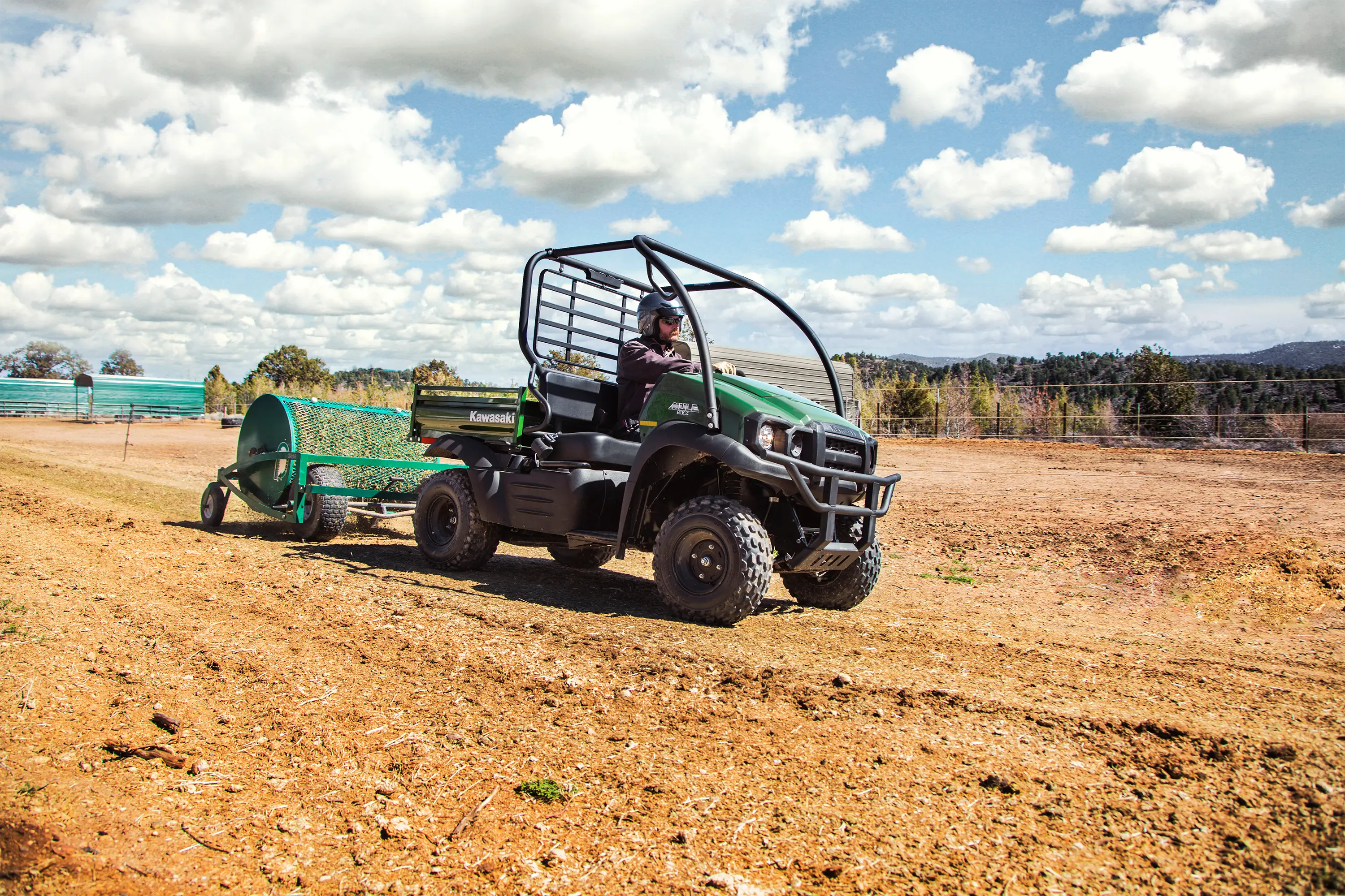 Front three-quarter angle of a person in a side x side towing a trailer through a field.