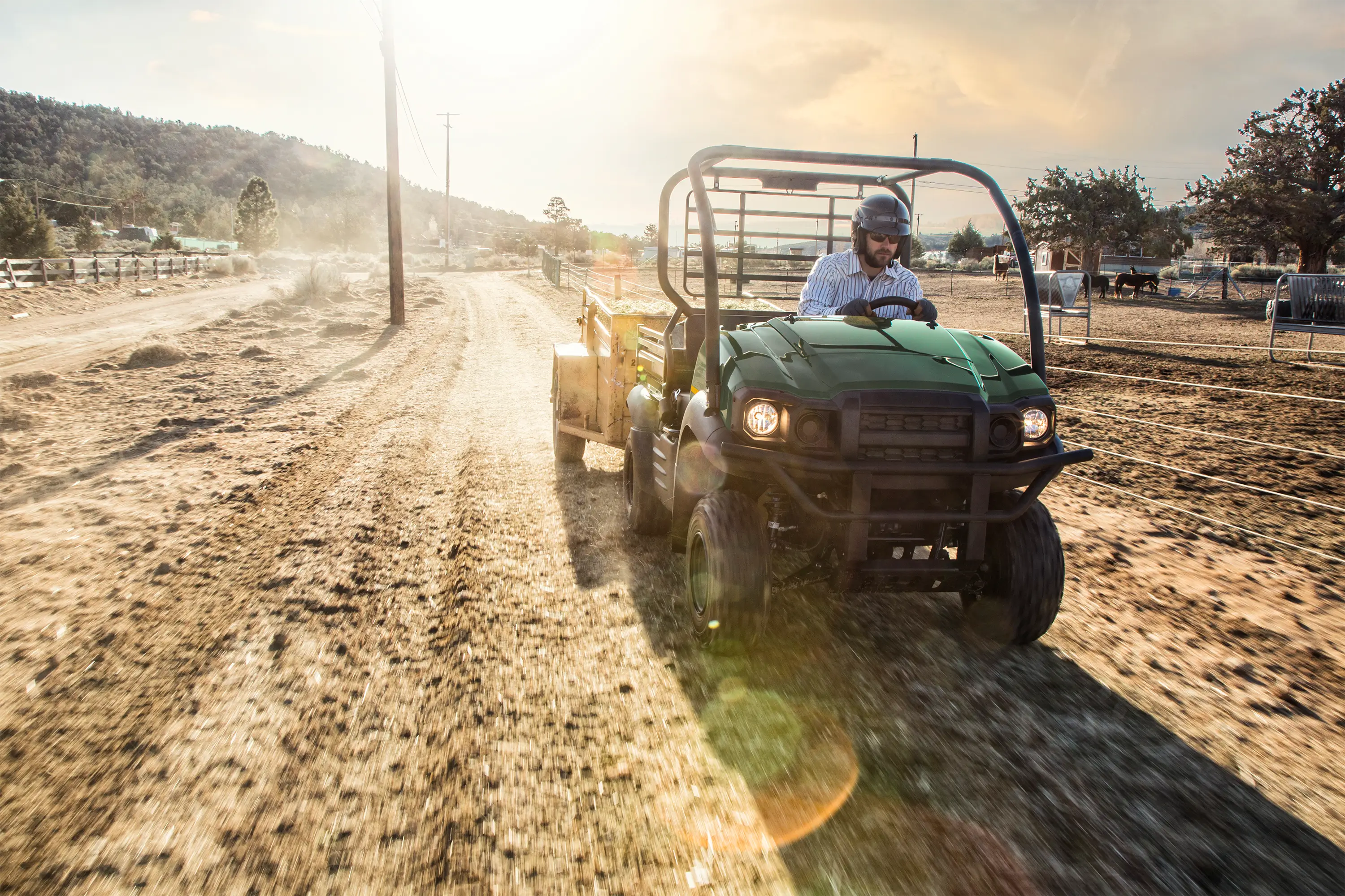 Front angle of a person driving a side x side through a field backlit by the sun.