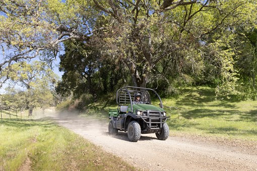 Front three-quarter view of a person driving a side x side on a dirt road lined by trees. opens in a new window