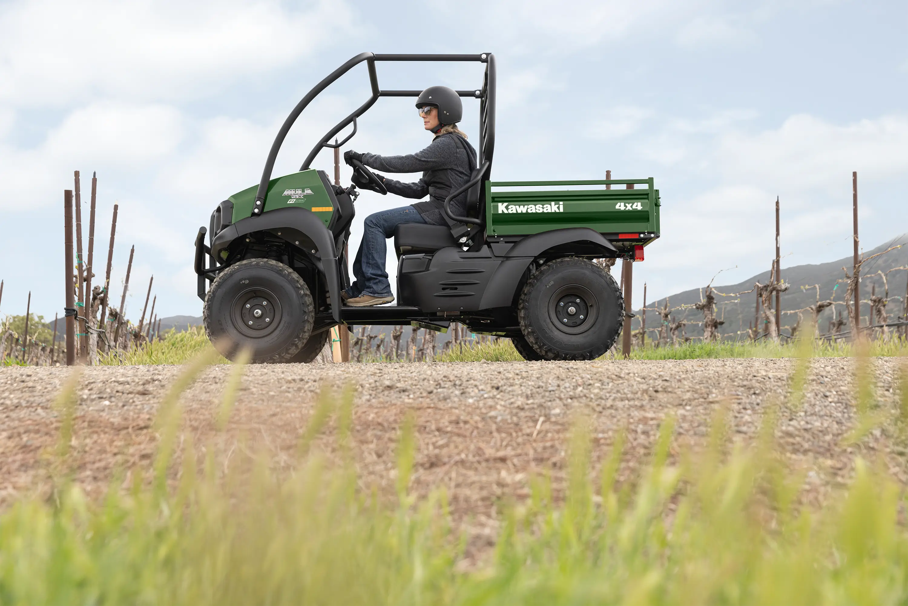Side view of a person driving a side x side through a grassy field.