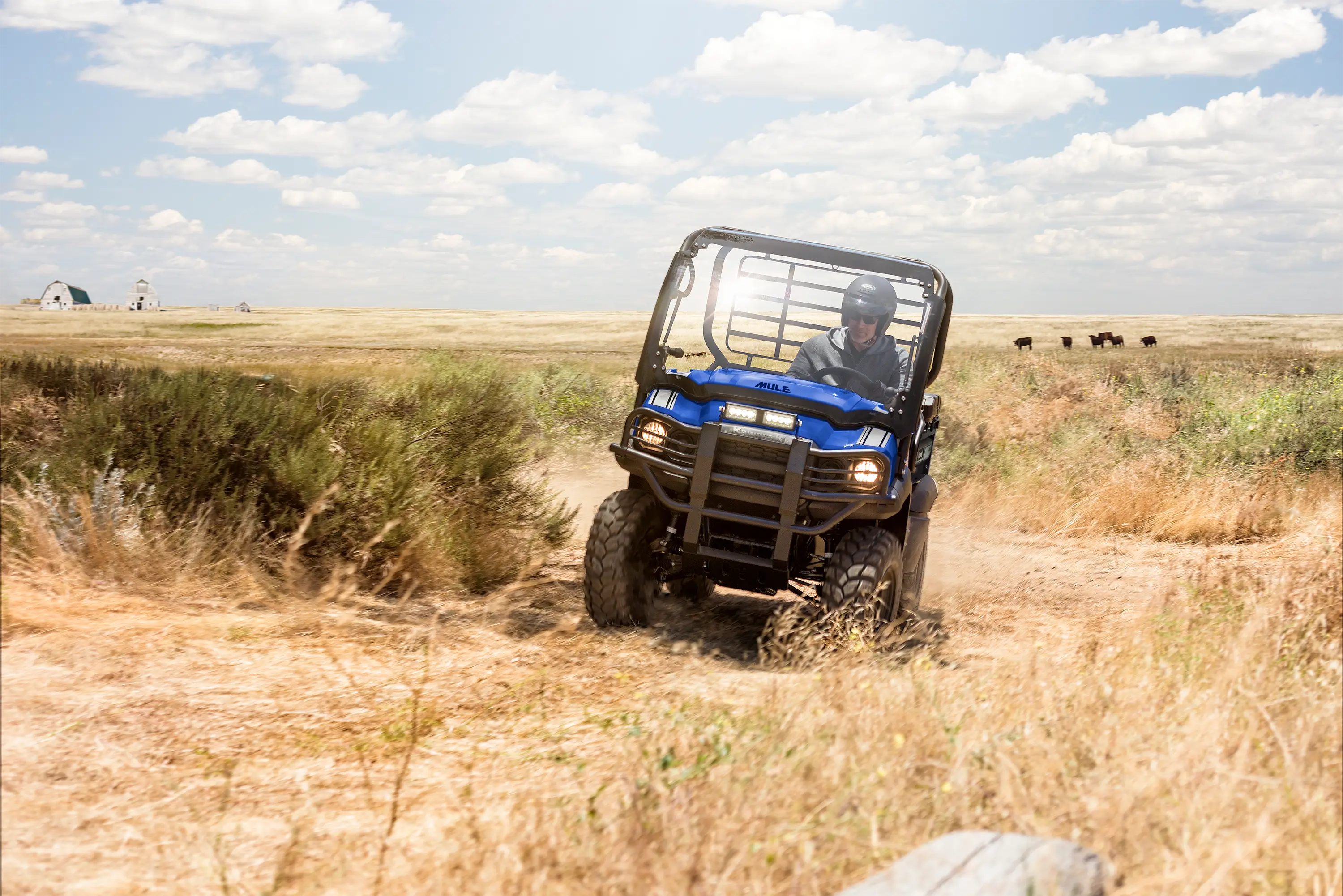 Front view of a person driving a blue side x side around a turn through an agricultural farm.