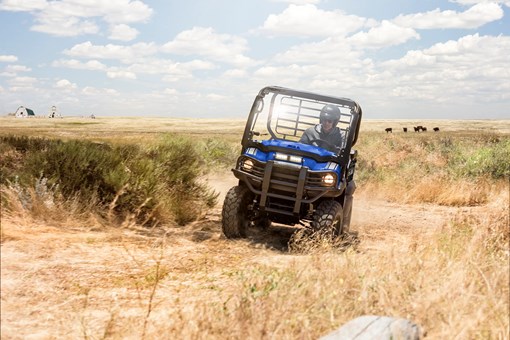 Front view of a person driving a blue side x side around a turn through an agricultural farm. opens in a new window