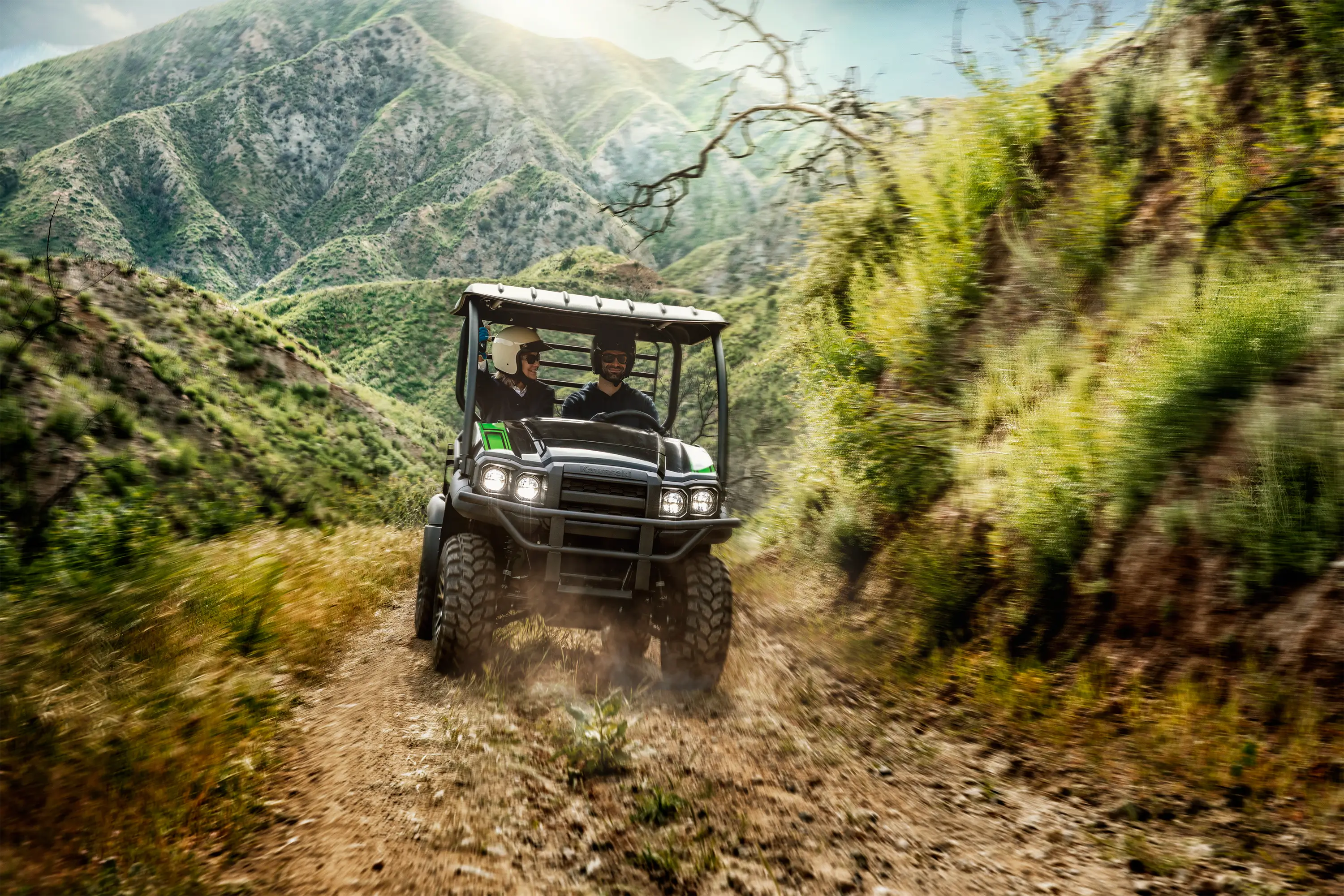 Two people riding on a rocky dirt road through the mountains in a side x side.