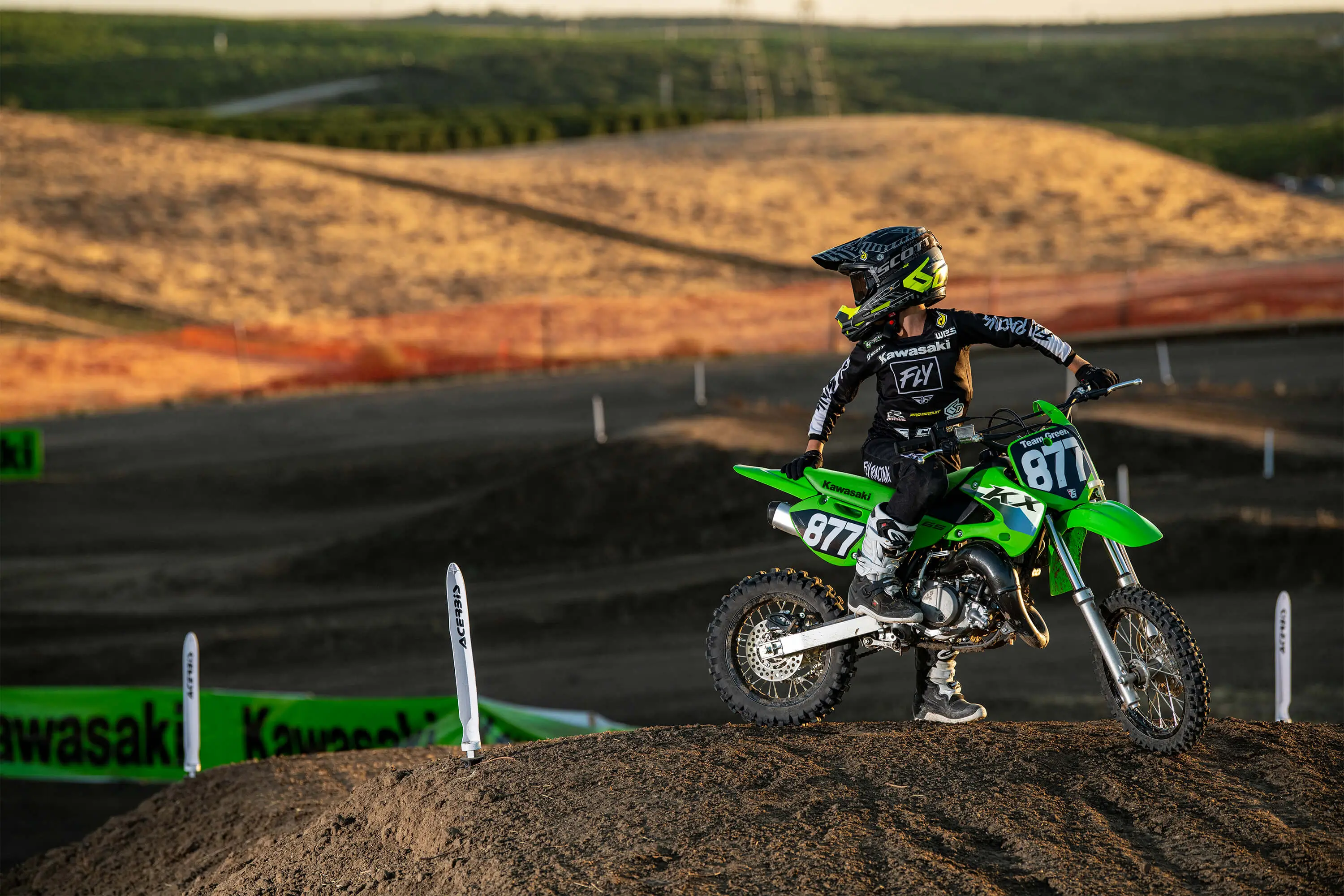 Kid parked on a green dirt bike on a motocross bike looking over his shoulder.