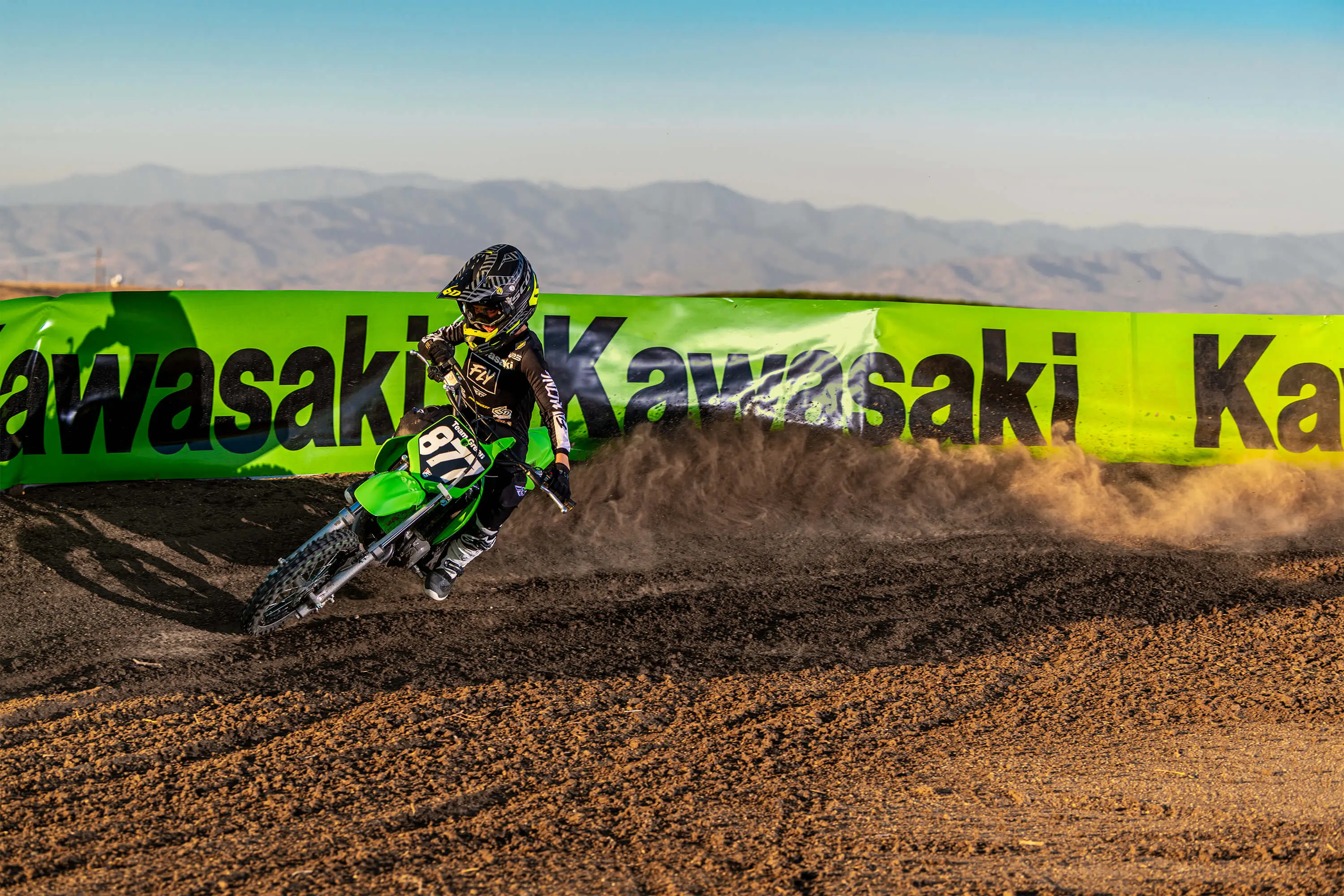 Front three-quarter view of a kid on a youth motocross dirt bike riding through a turn.