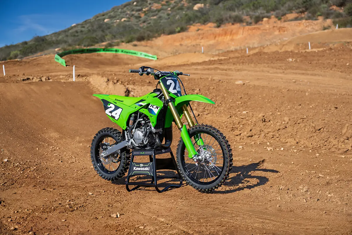 Right side view of a green dirt bike parked on a dirt motocross track.