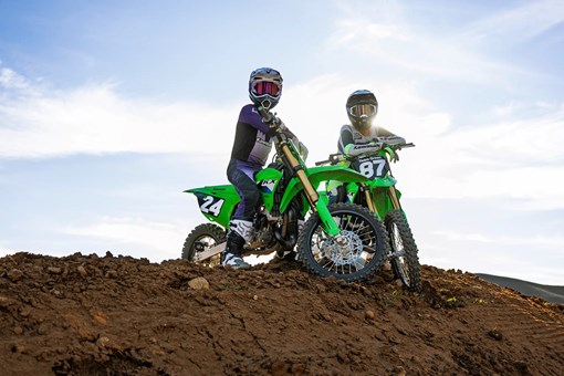 Oncoming view of a person riding a green dirt bike fast on a motocross track through a turn. opens in a new window