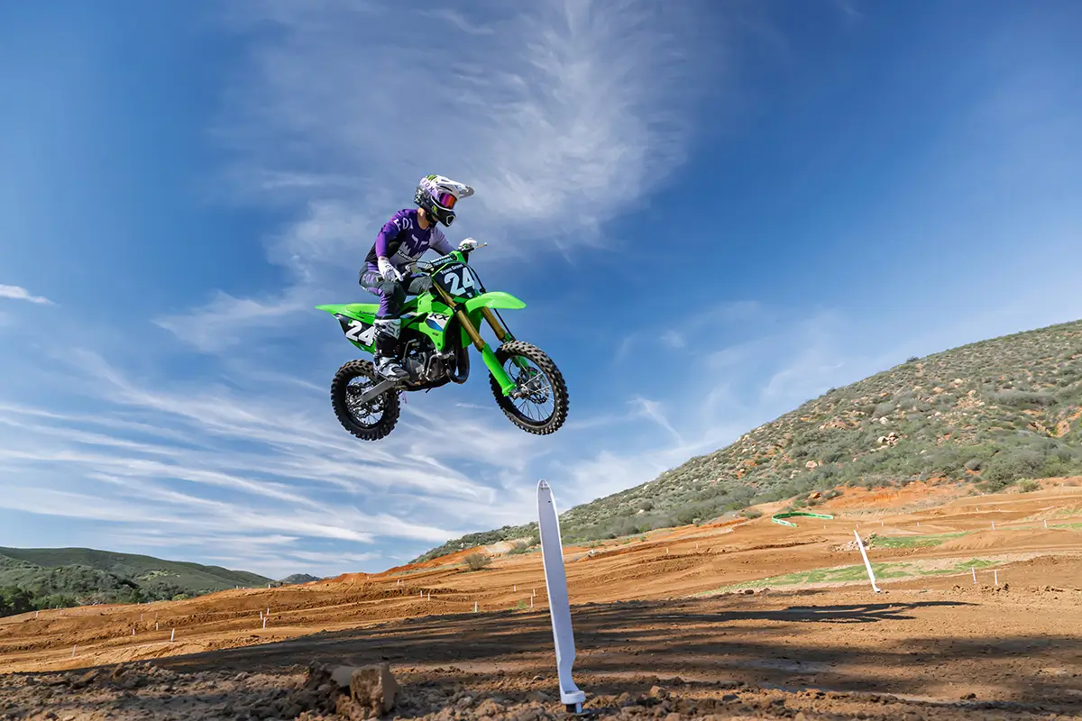 Right side view of a person jumping a green dirt bike on a motocross track.
