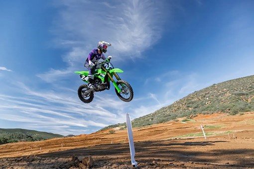 Right side view of a person jumping a green dirt bike on a motocross track. opens in a new window