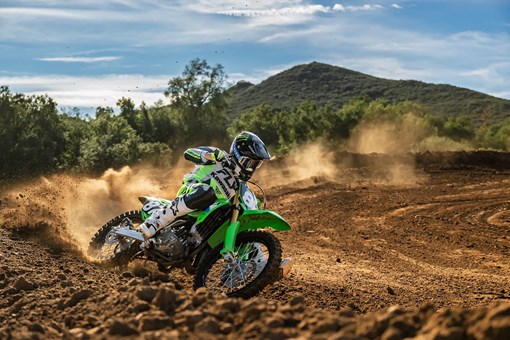 A person riding a green dirt bike fast around a dusty turn on a motocross track. opens in a new window