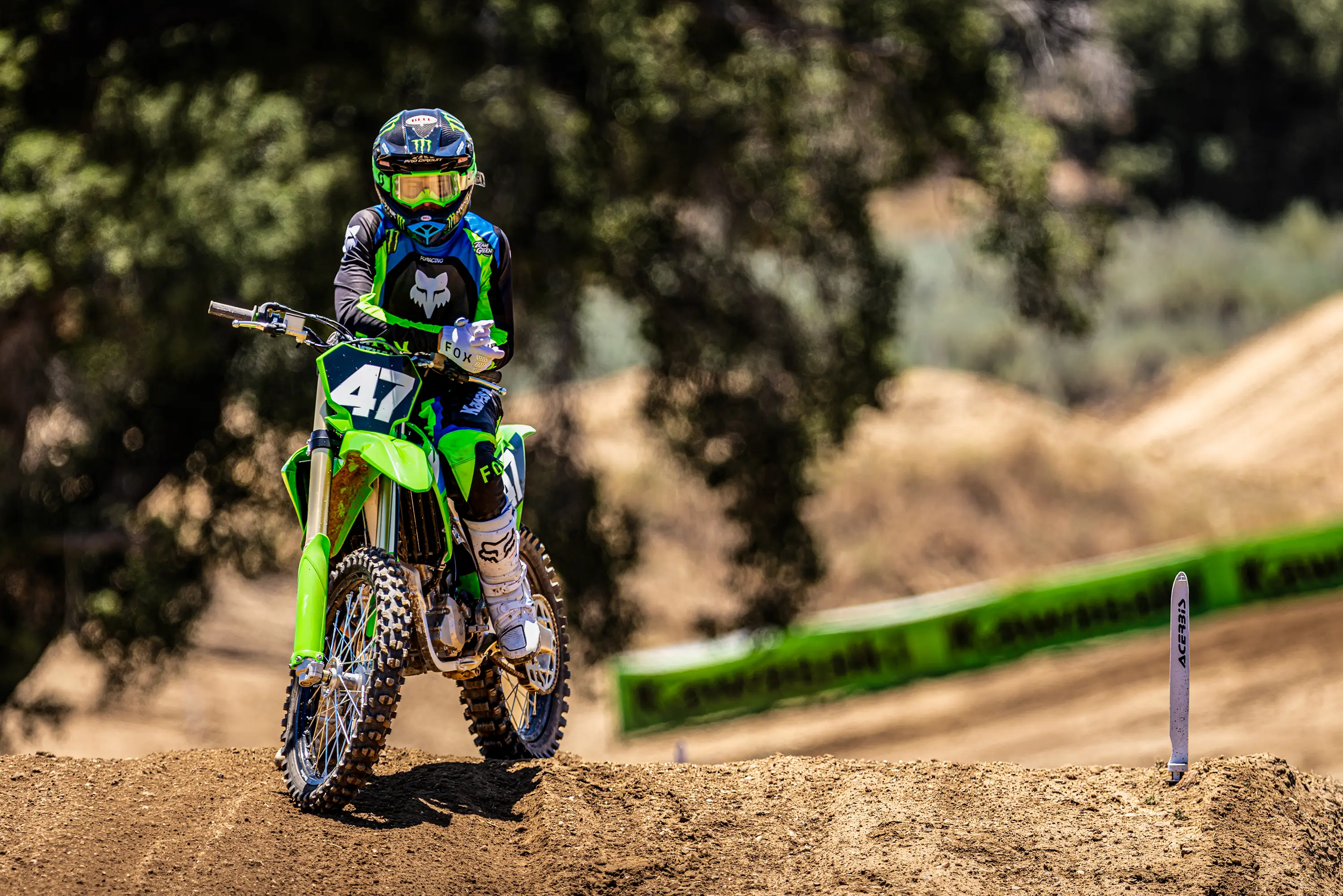 Front angle of a person seated on a motorcycle on a dirt track.