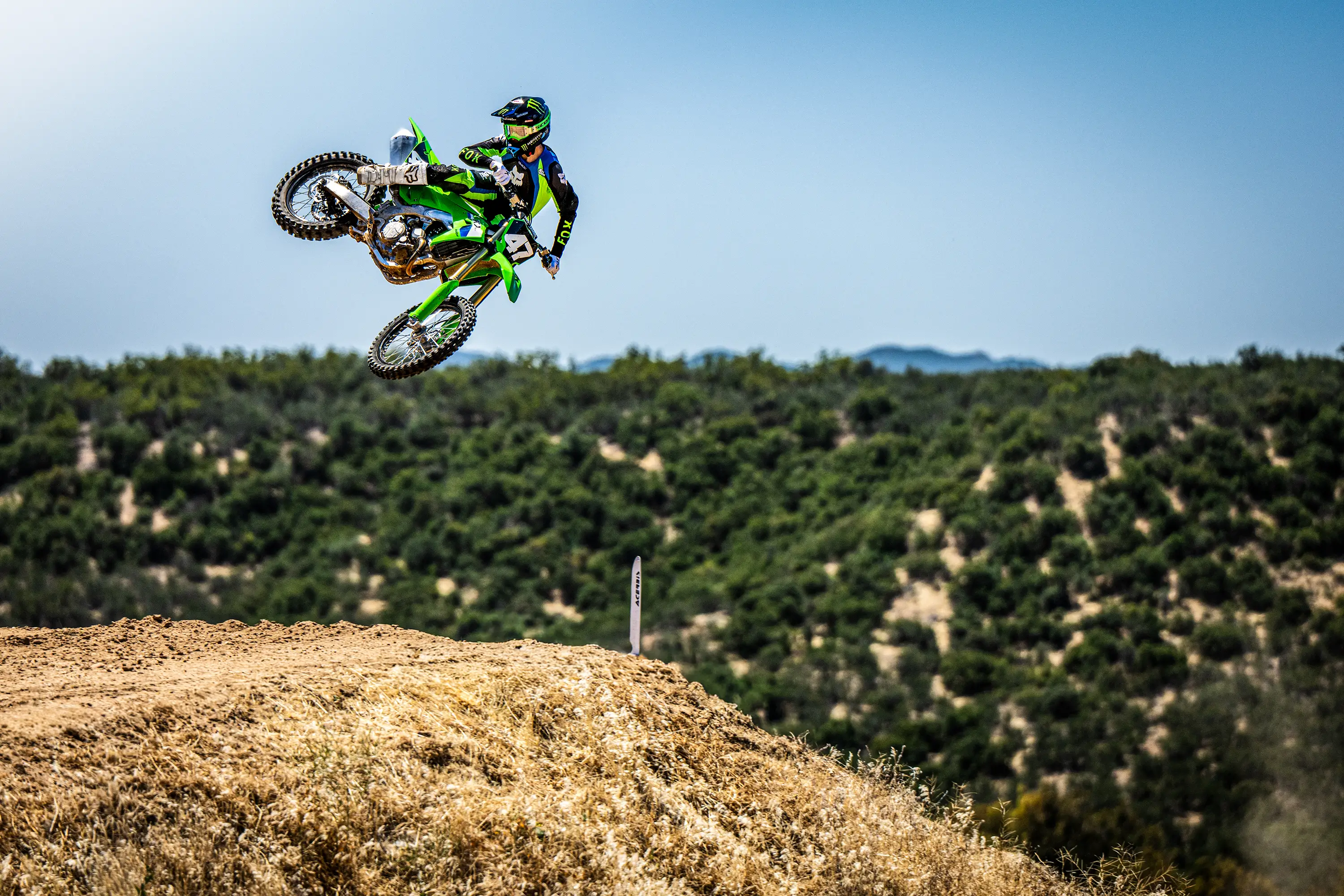 Three-quarter front angle of a person riding a motorcycle over a jump on a dirt track.