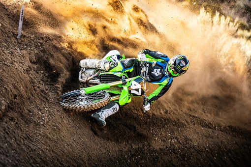 Front angle of a person riding a motorcycle around a bend on a dirt track. opens in a new window