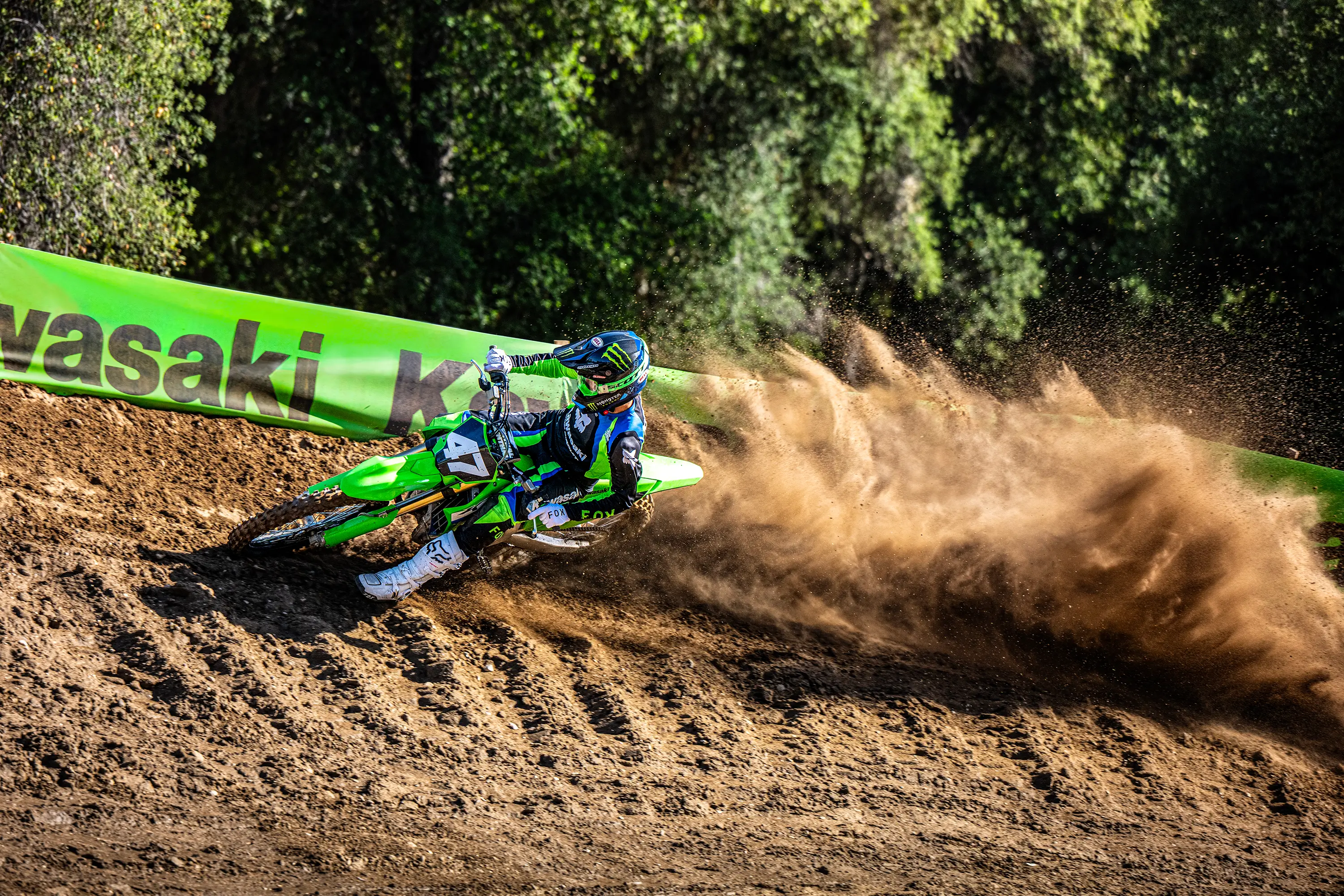 Three-quarter front angle of a person riding a motorcycle around a bend on a dirt track.