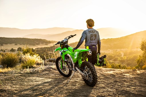 Three-quarter rear angle of a person standing next to a motorcycle parked at a dirt overlook. opens in a new window