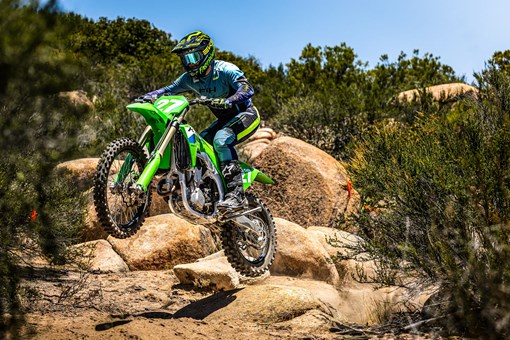 Side angle of a person riding a motorcycle over a jump on an off-road trail. opens in a new window