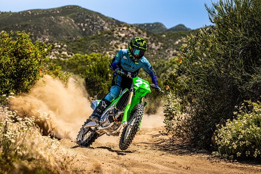 Three-quarter front angle of a person riding a motorcycle on a dirt path. opens in a new window