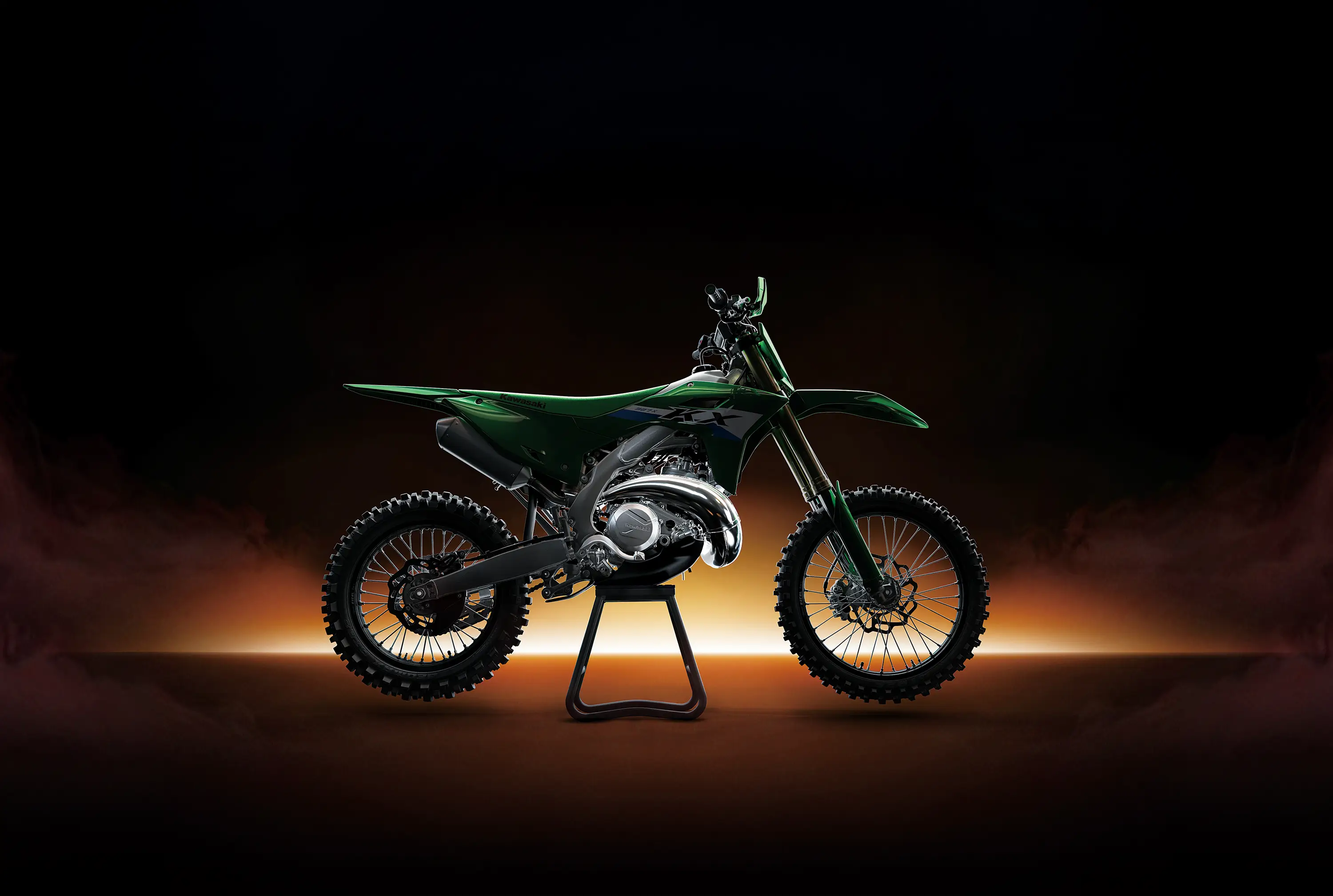 Right side view of a green dirt bike in a black studio background with glowing yellow backlighting.